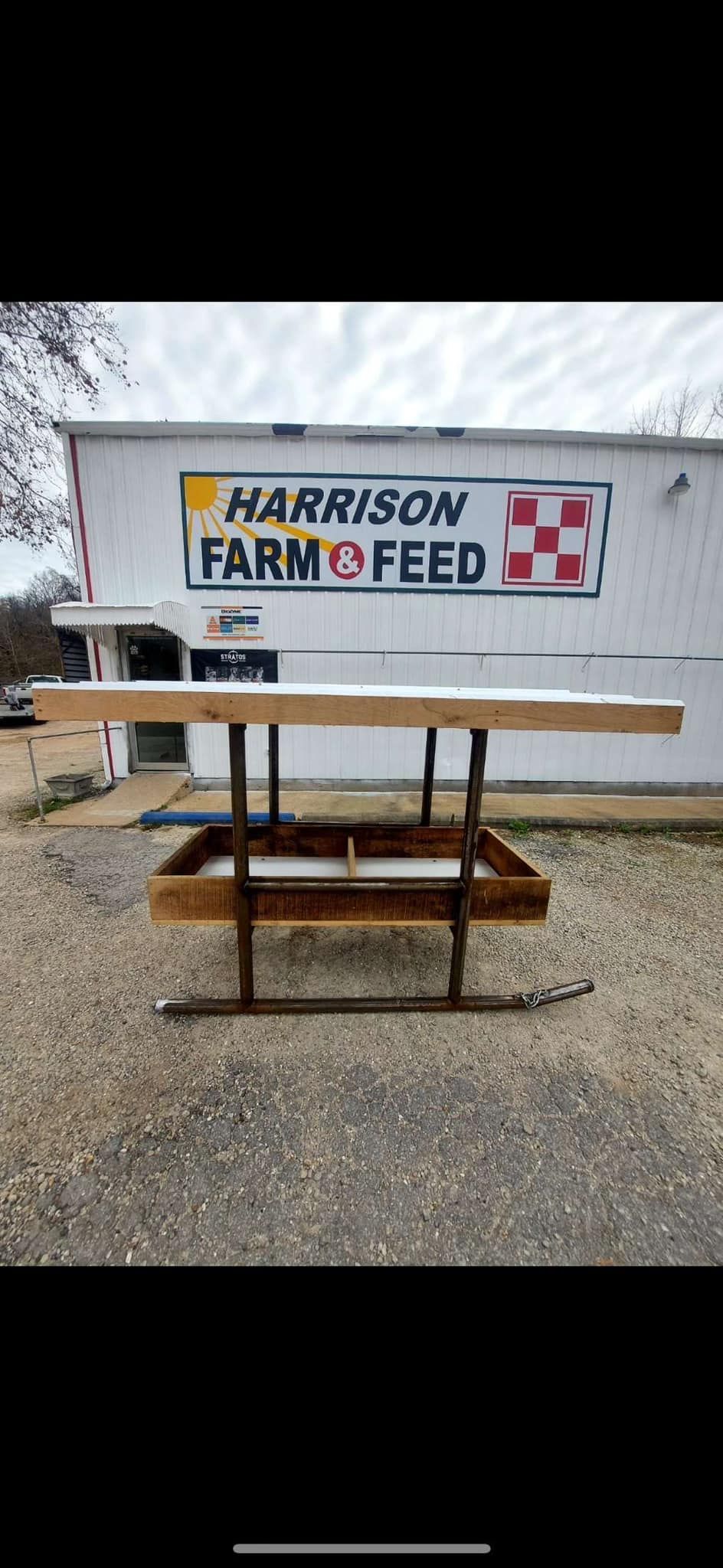 A wooden farm feeder in front of the Harrison Farm Feed store.