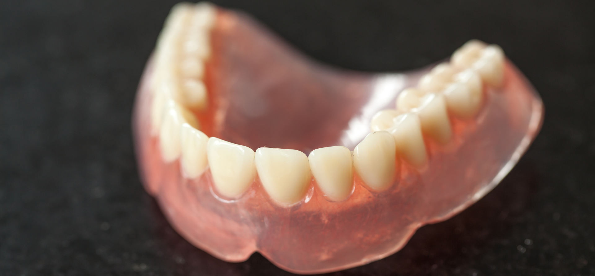 A close up of a denture with teeth on a black surface.
