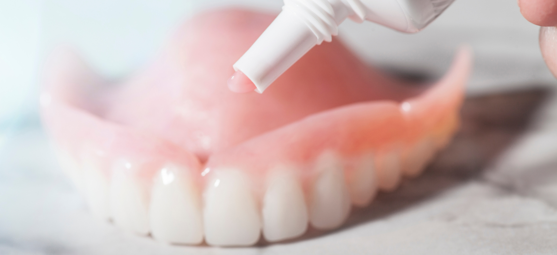 A person is applying toothpaste to a denture.
