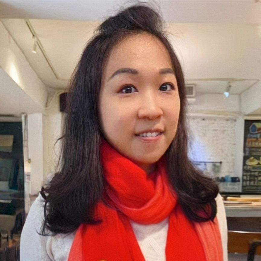 深色頭髮、戴著紅色圍巾、微笑的女子。室內，中性背景。