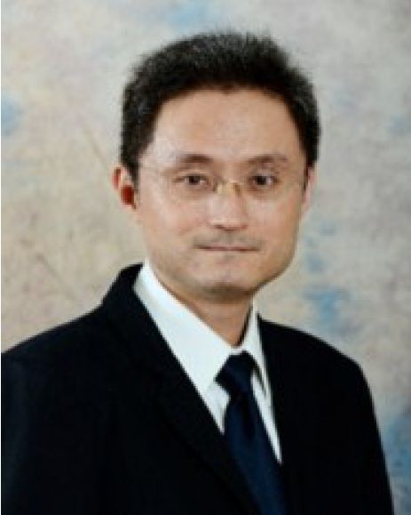 一名男子身穿深色西裝，繫著領帶，戴著眼鏡。他有著黑髮，面帶微笑。