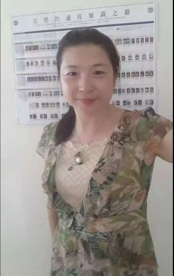 穿著花裙的女子在一張寫有漢字的海報前微笑。