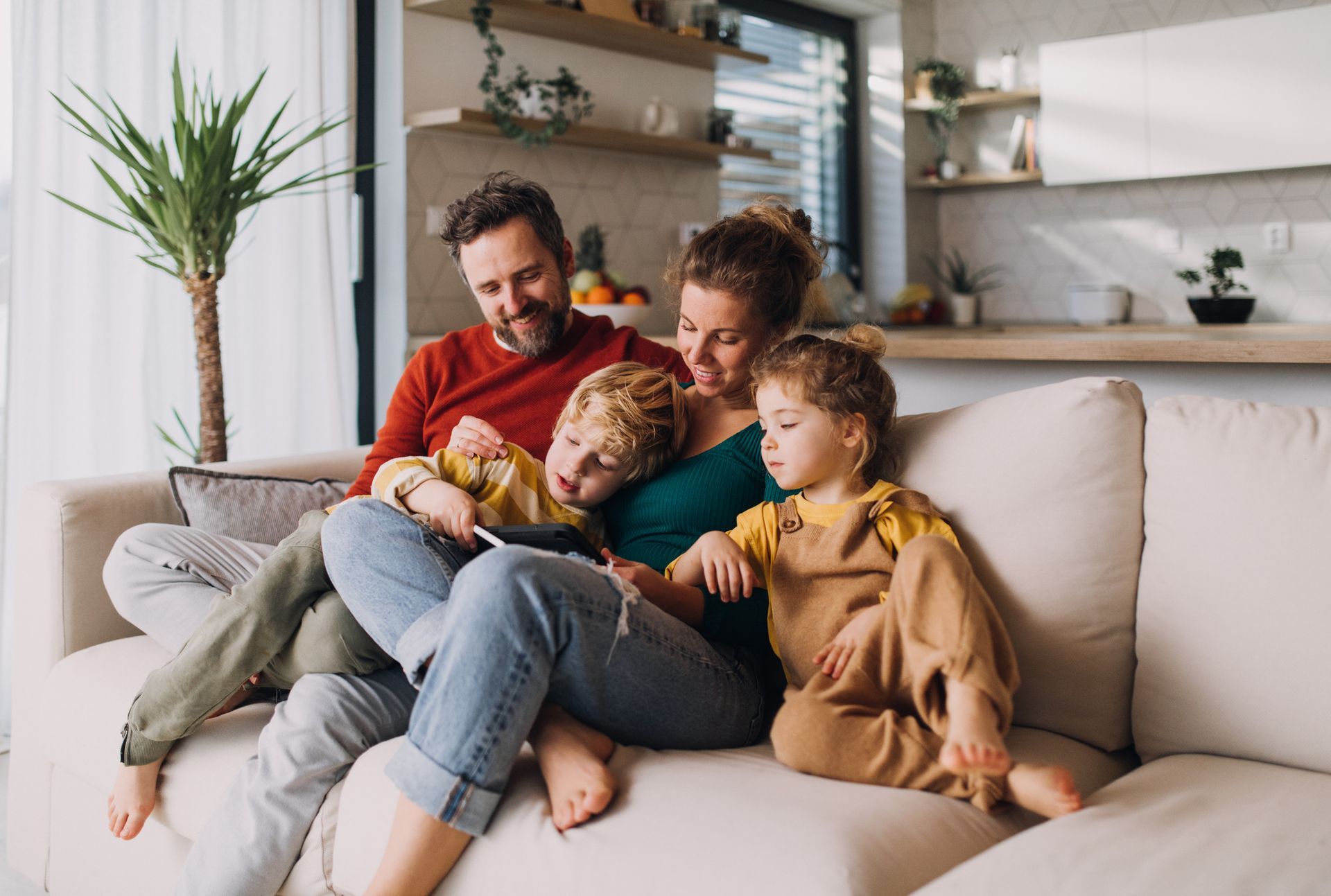 A family is sitting on a couch looking at a tablet.