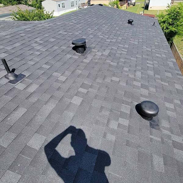 A man is standing on top of a roof with his shadow on it.