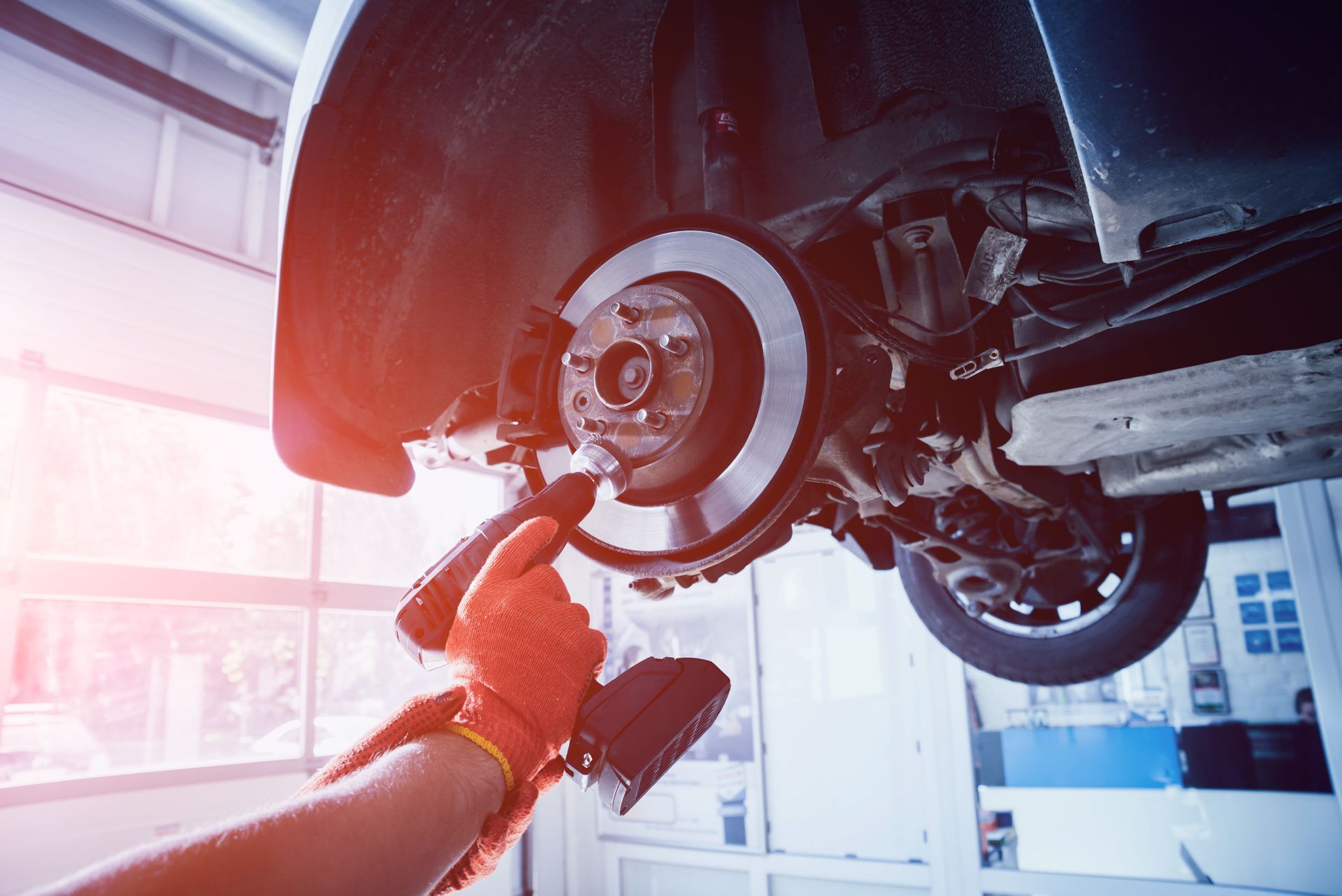 Mechanic using a power tool to work on a car’s exposed brake disc on a lift.