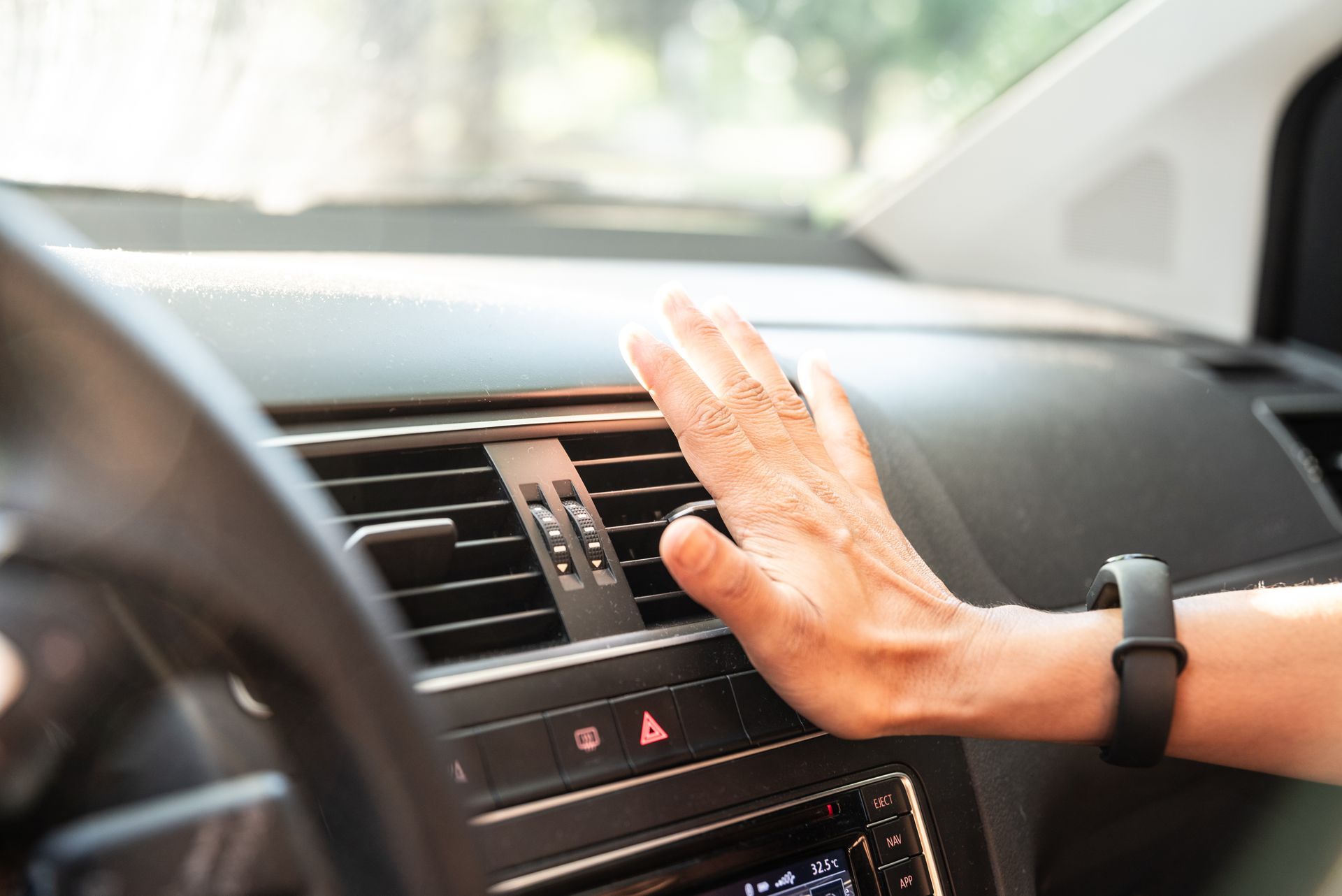Hand testing car's air conditioning vent. Interior shot, focus on dashboard with black vents and a smartwatch on the wrist.