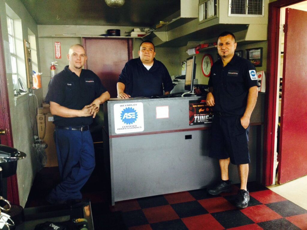 Three auto mechanics pose behind a counter in a shop.