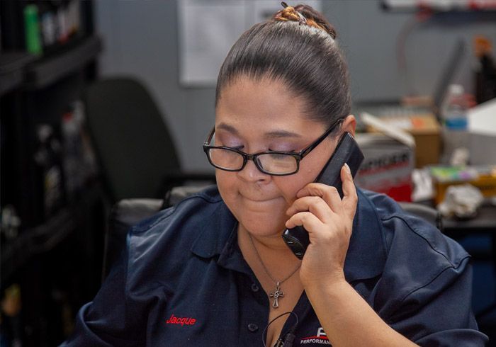 Woman in blue shirt on phone, wearing glasses, at a desk indoors.