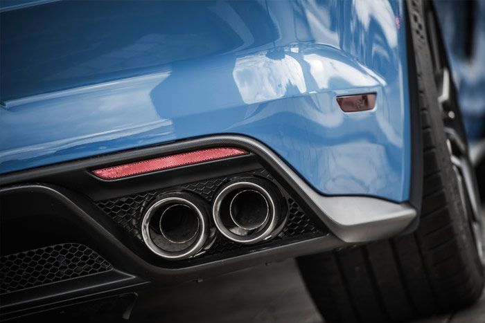 Close-up of a blue car's rear, showcasing dual exhaust pipes and a red reflector.