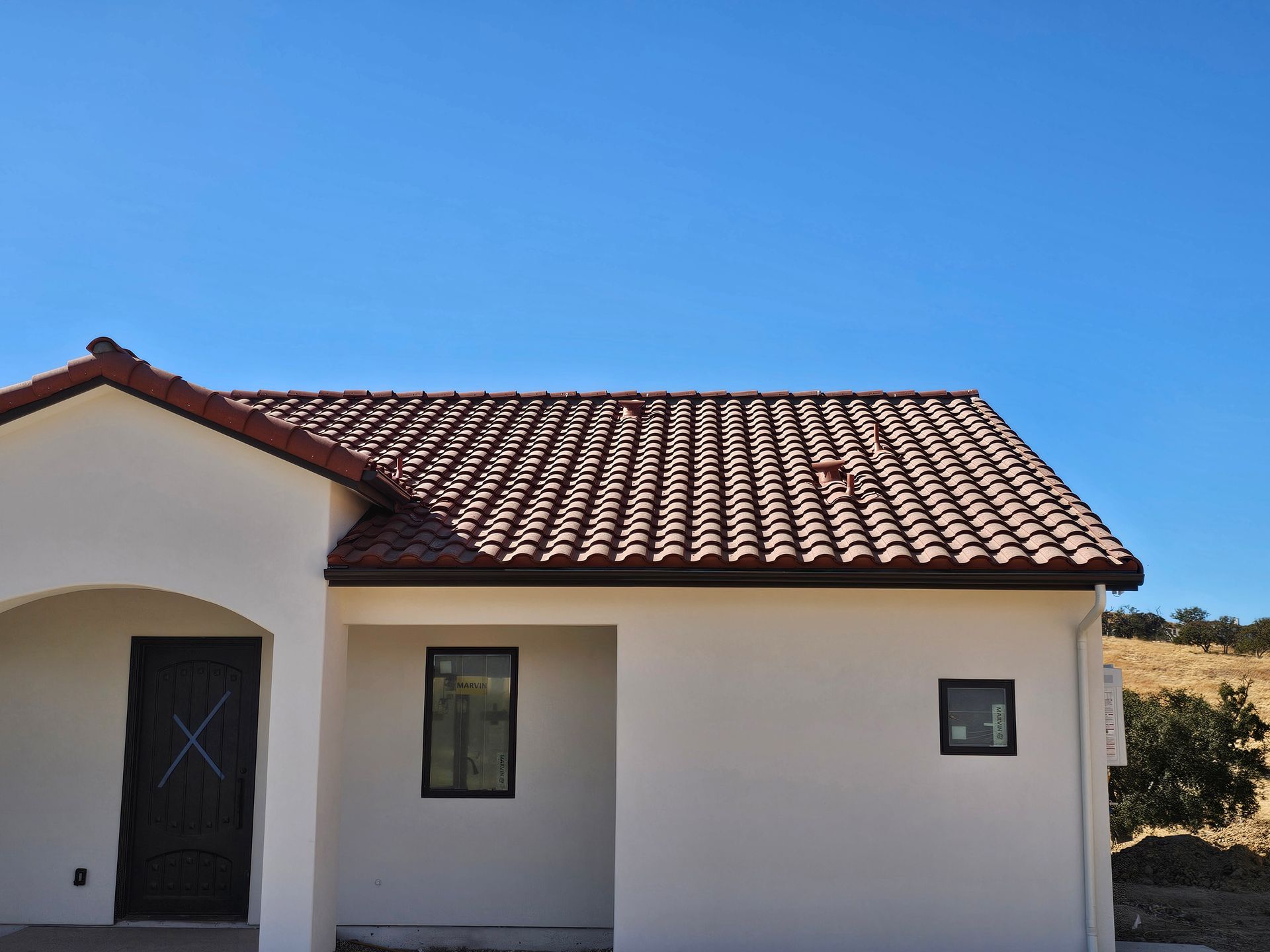 A gutter on the side of a house with trees in the background.