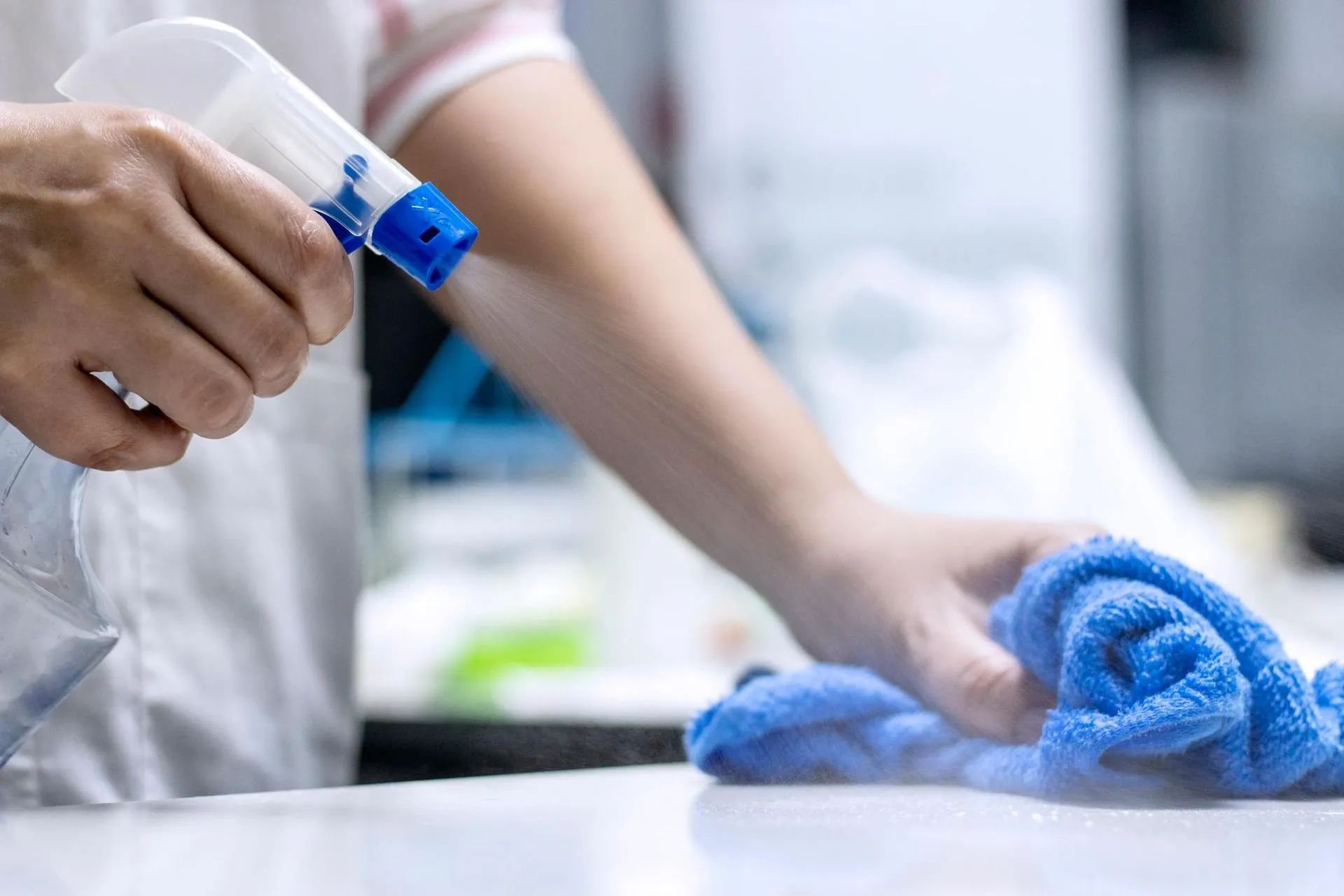 a person is cleaning a table with a spray bottle and a towel