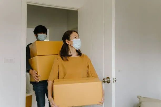 a man and a woman wearing face masks are carrying boxes into a new home