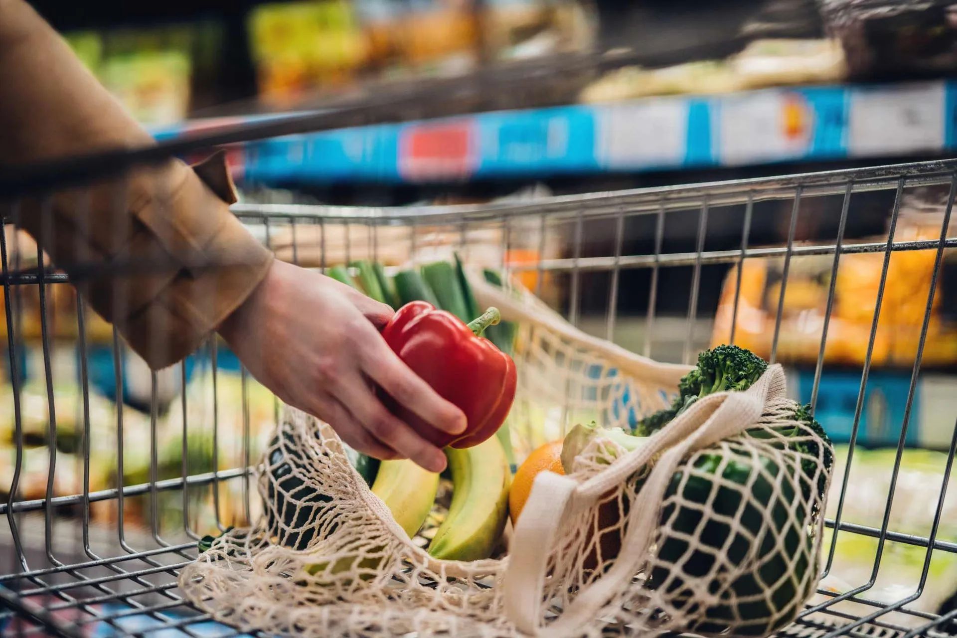 a person is putting a red pepper in a shopping cart filled with vegetables