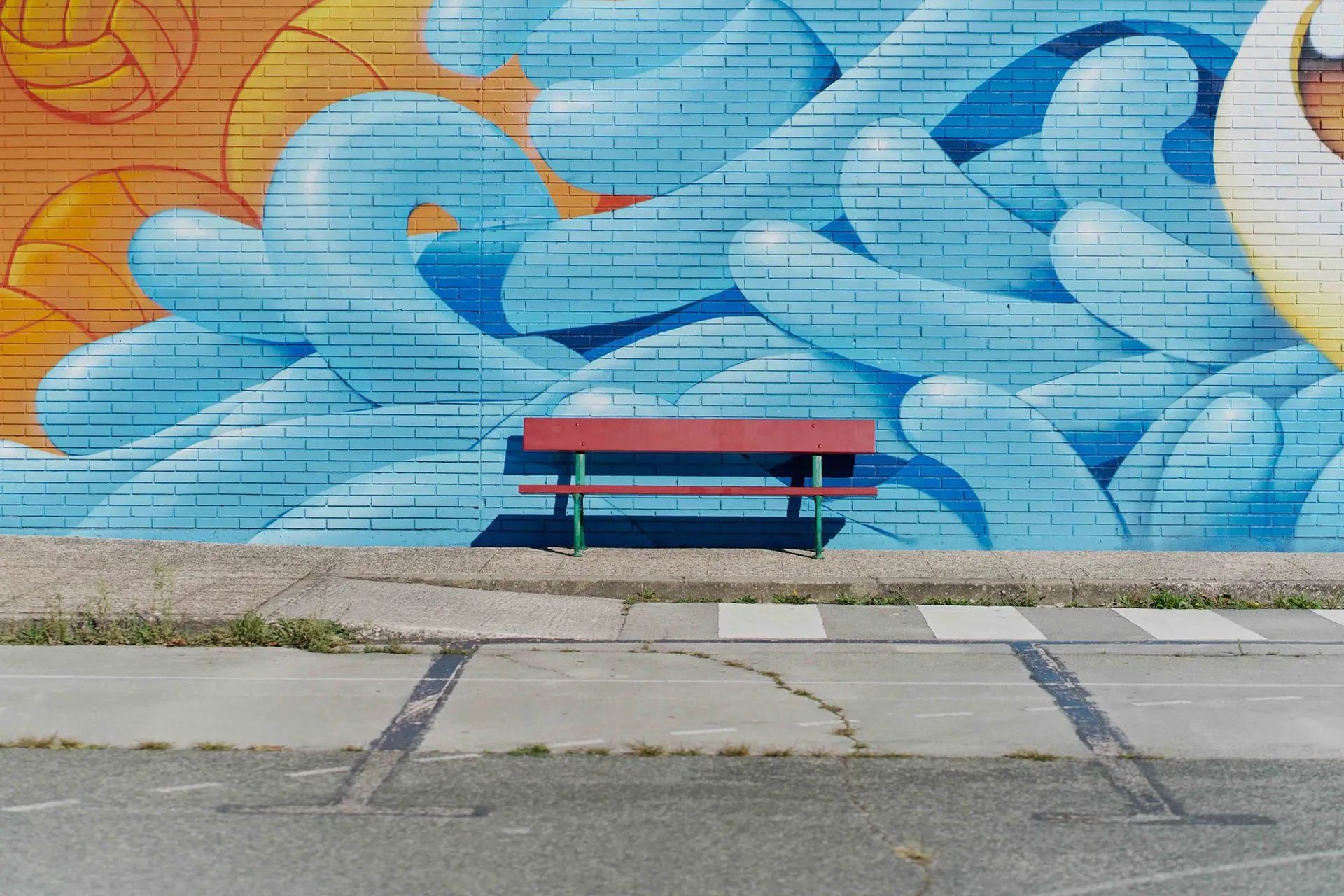 a red bench is sitting in front of a mural on a brick wall