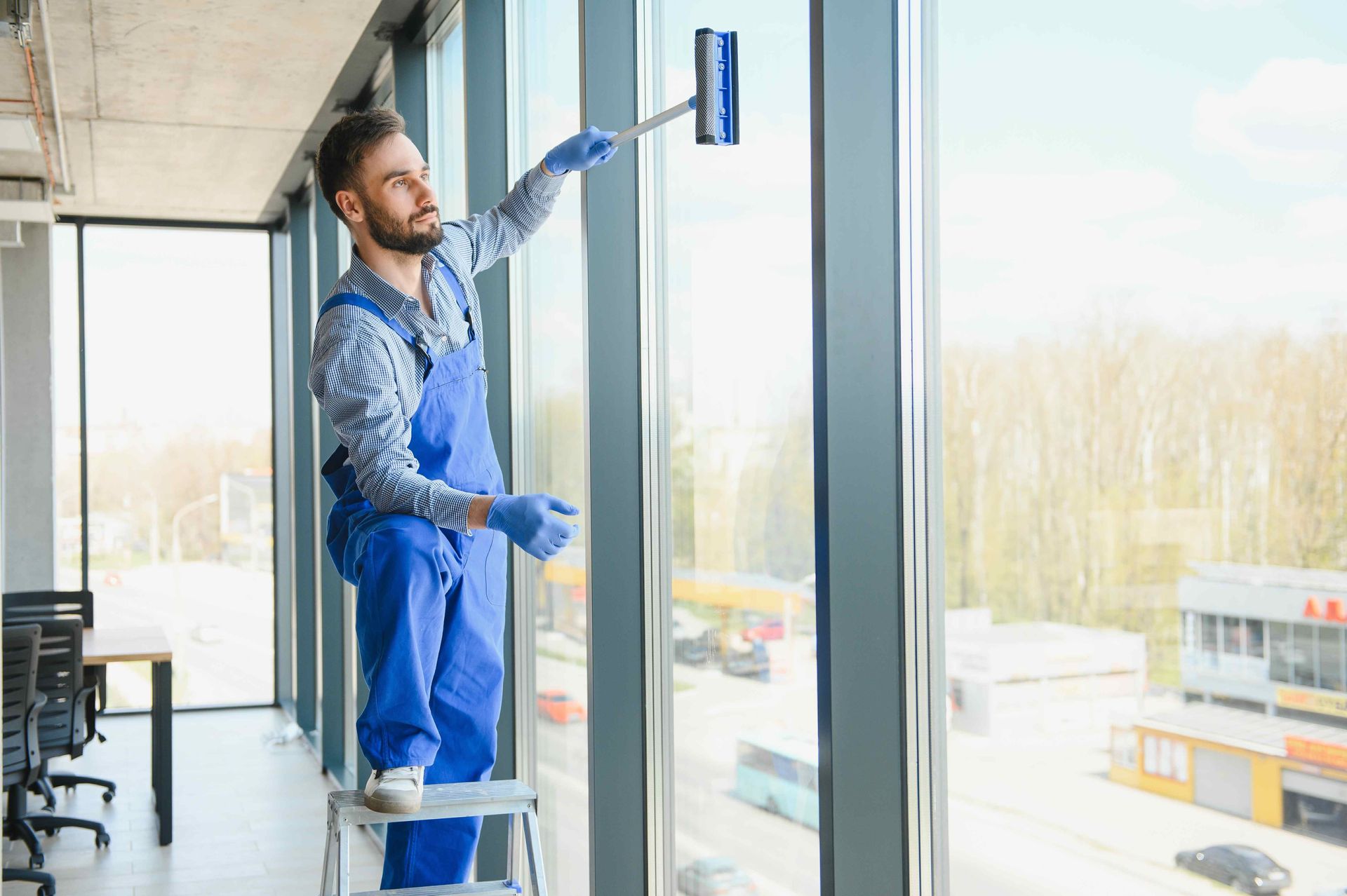 a man is standing on a ladder cleaning a window in an office .