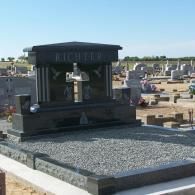 A black granite gravestone with a cross engraving and the name 
