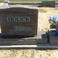 A brown granite headstone in a cemetery with the name 