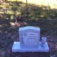A gray stone grave marker in a grassy field, inscribed with the name 