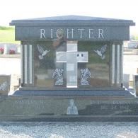 A black granite family mausoleum with a large central cross, etched doves, and the name 