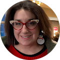 A woman wearing glasses and earrings is smiling in a circle.