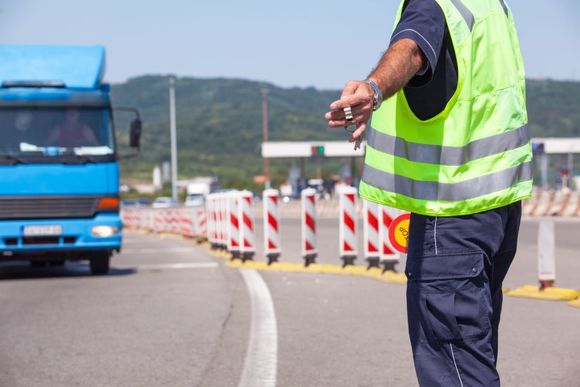 A traffic officer in a neon vest directs a blue truck at a toll booth.