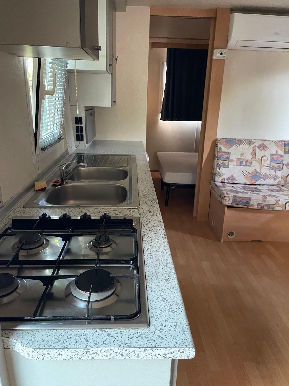 Una cucina compatta con piano cottura a gas a quattro fuochi e lavello, che si apre su una piccola zona giorno con una panca imbottita.