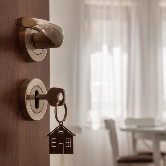 Door lock with key and house-shaped keychain, with a softly lit room in the background
