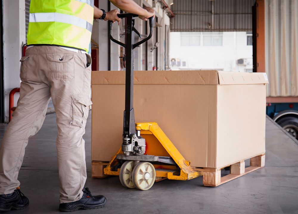 A man is pushing a pallet jack with a box on it in a warehouse.