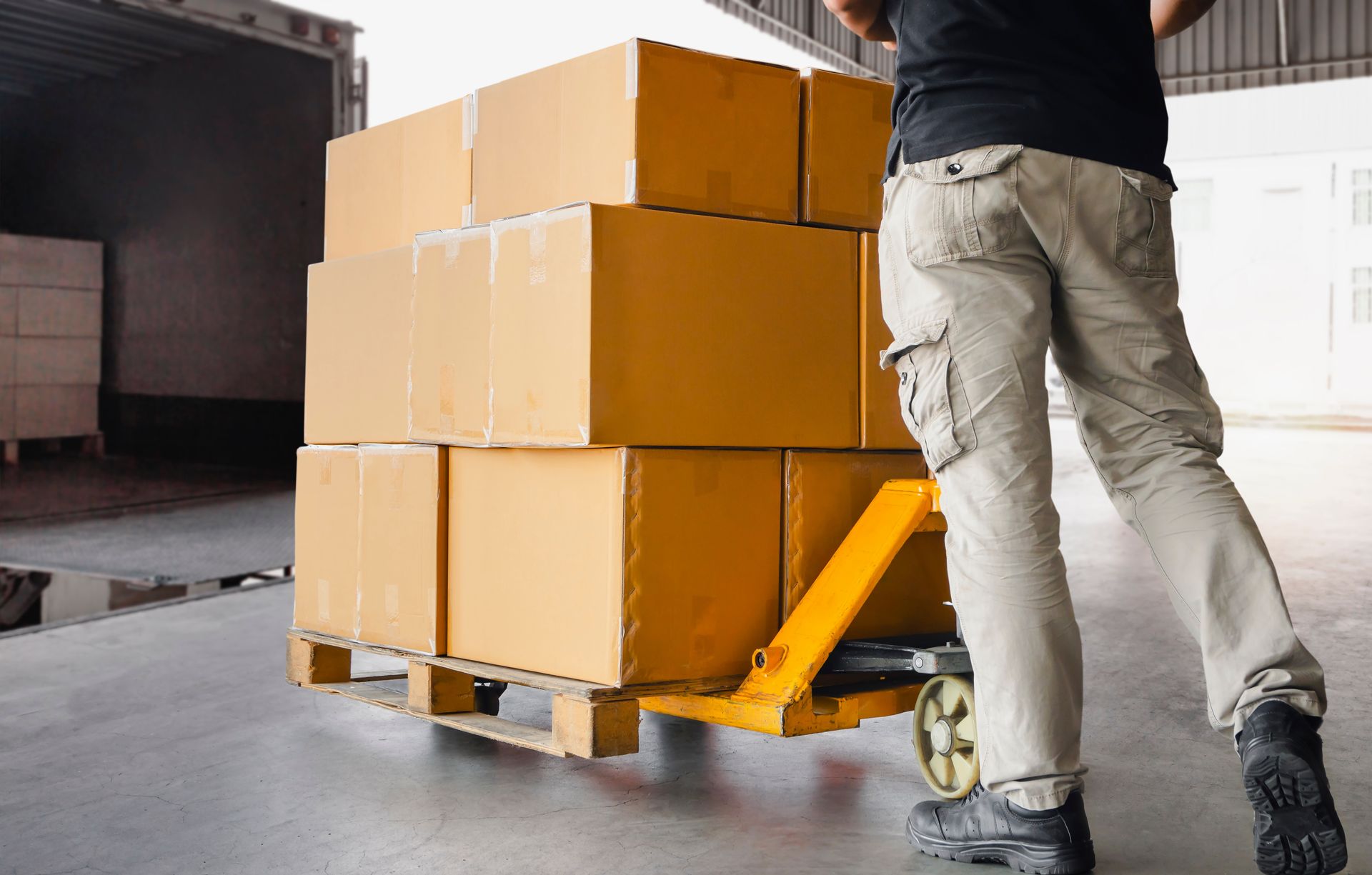 a man is pushing a properly loaded pallet with boxes on it in a warehouse.