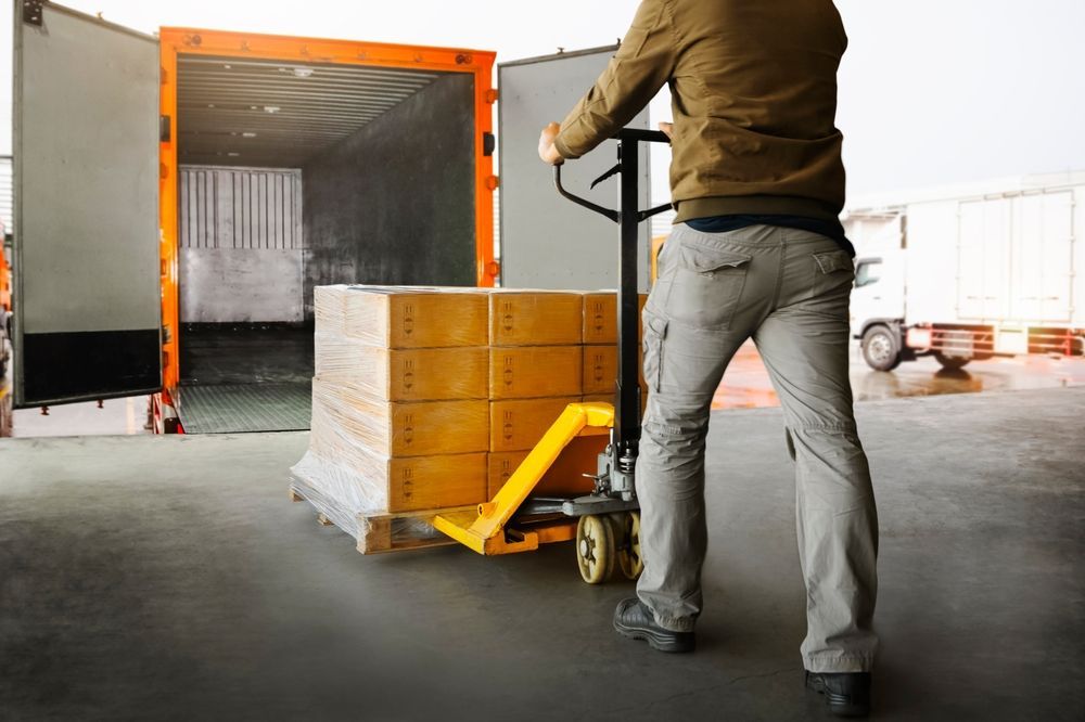 A man is pushing a pallet truck with boxes on it.