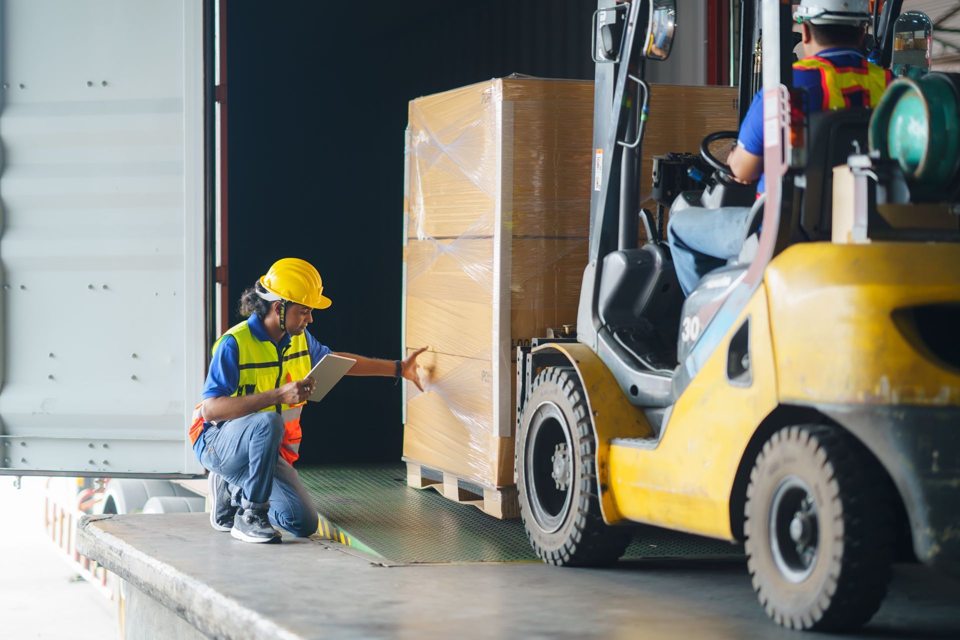 a warehouse employee inspects a pallet shipment on a forklift before it is placed in a semi truck