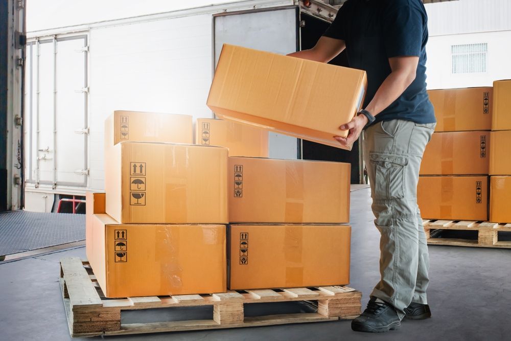 A man is loading boxes onto a wooden pallet in a warehouse.