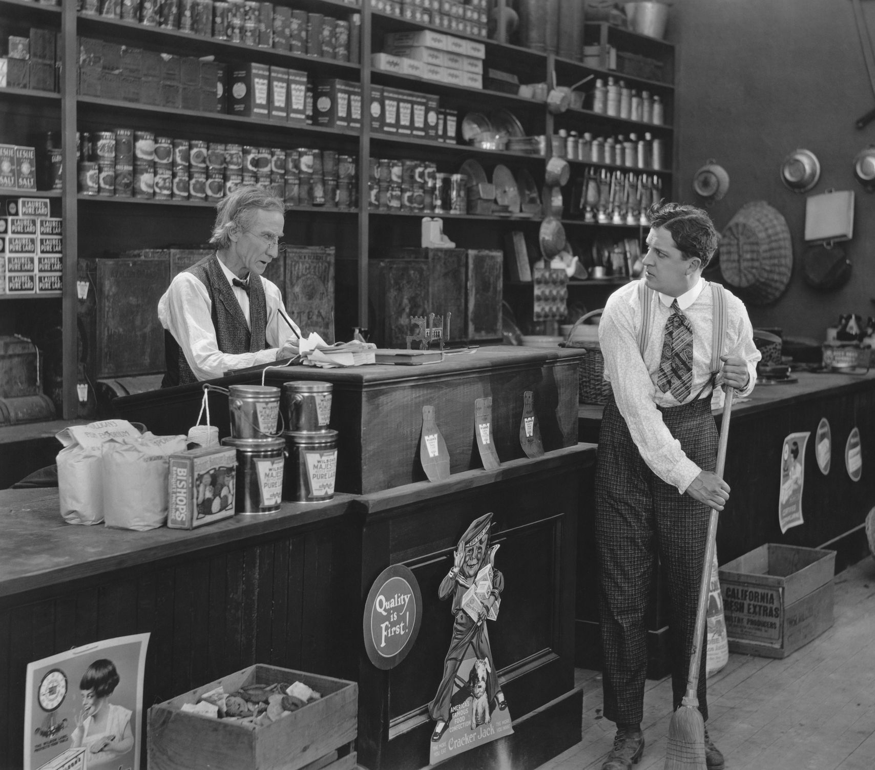 Vintage black and white photo, a stock boy in an old fashioned grocery store sweeping the shop floor during the standardization pallet sizes 