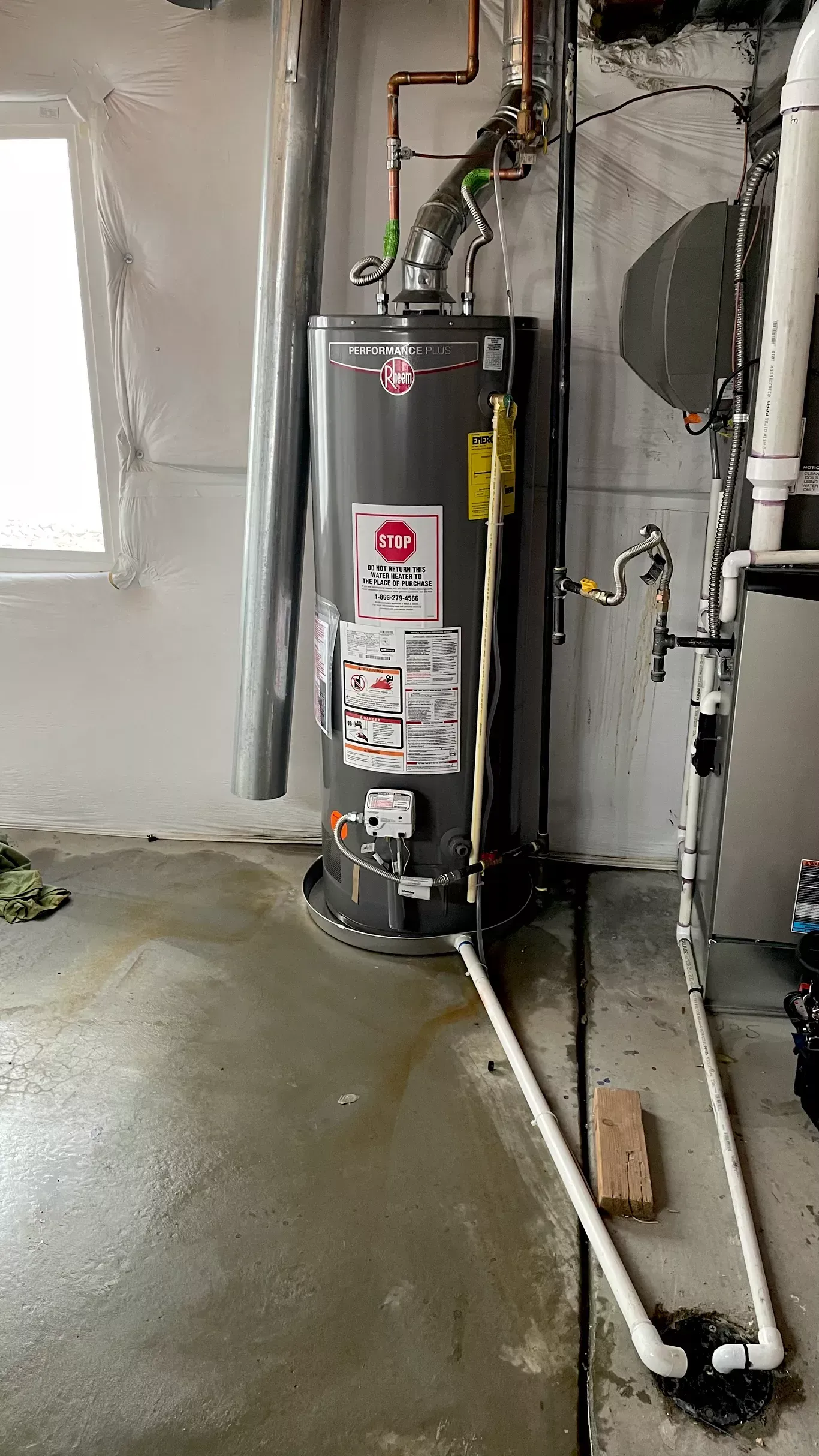 A gas water heater is sitting in a room next to a window.
