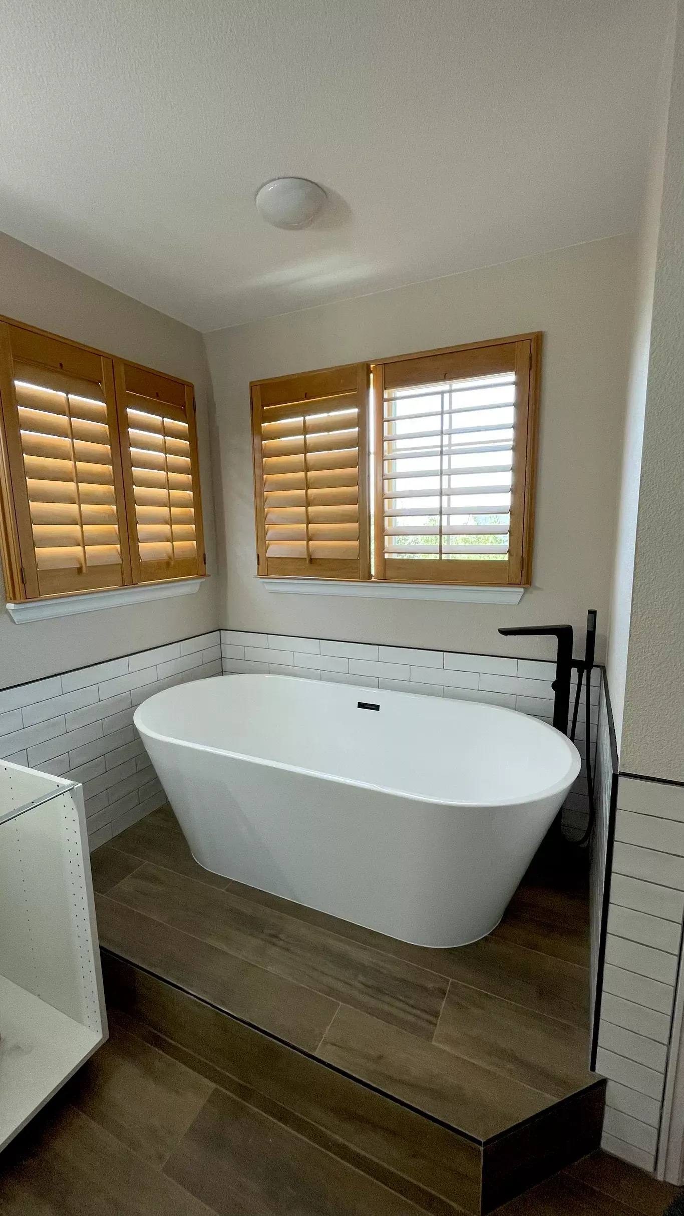 A bathroom with a bathtub and shutters on the windows.