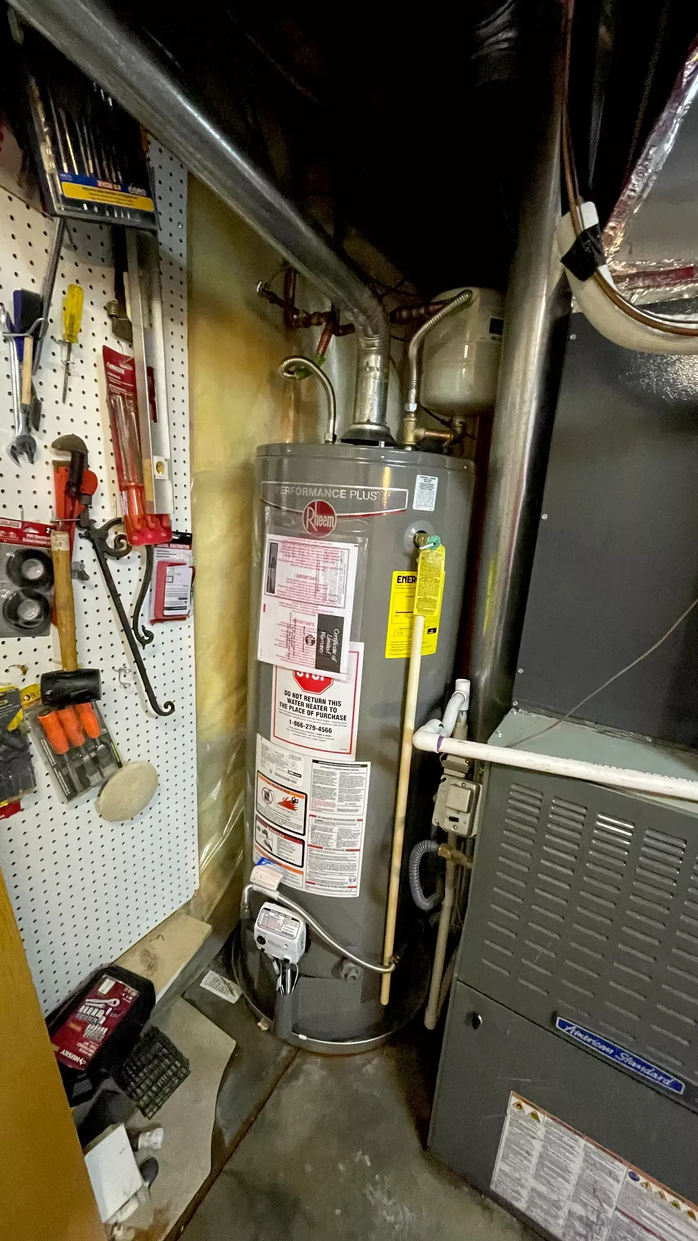 A water heater is sitting next to a furnace in a garage.