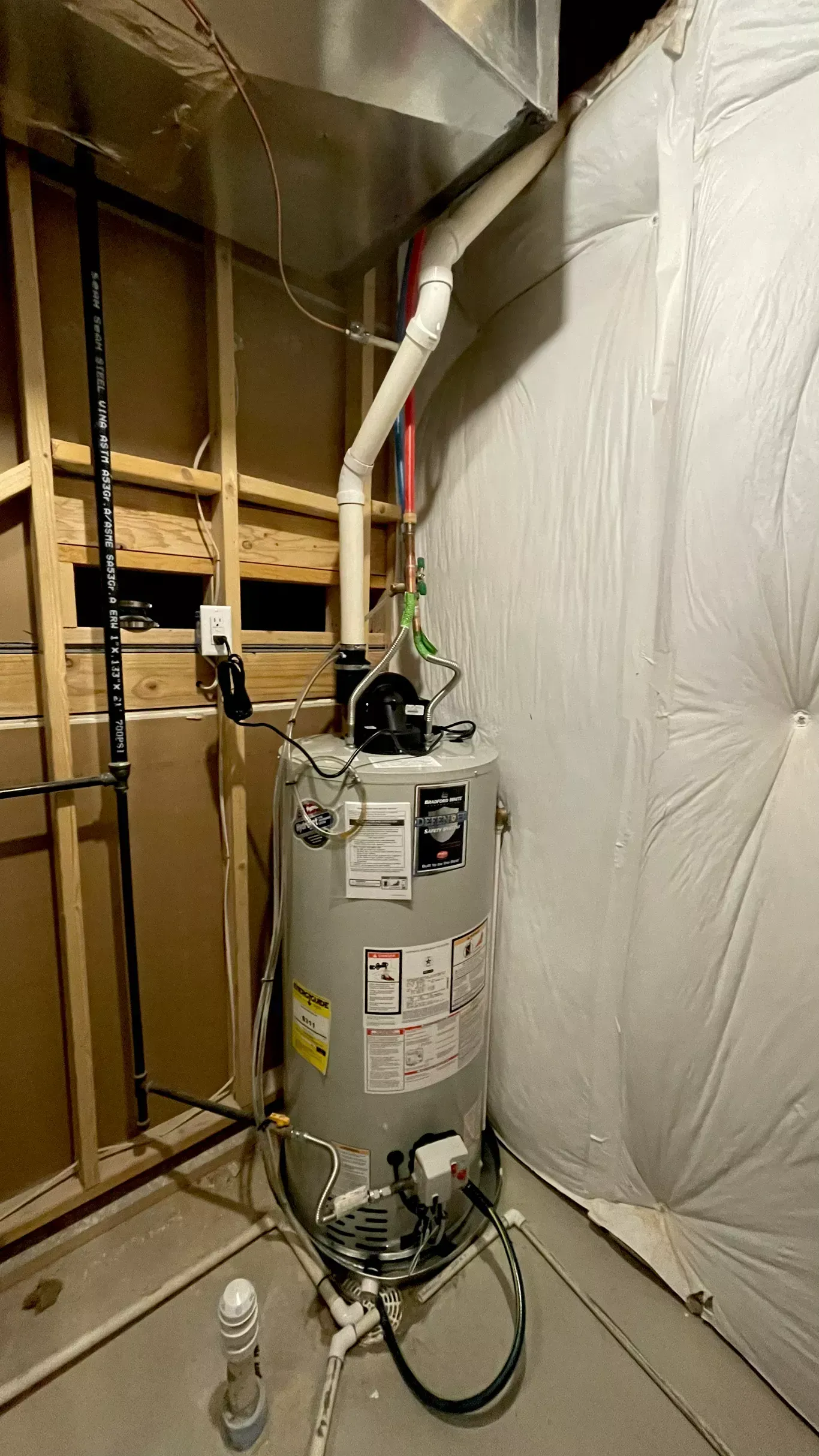 A water heater is sitting in a basement next to a wall.