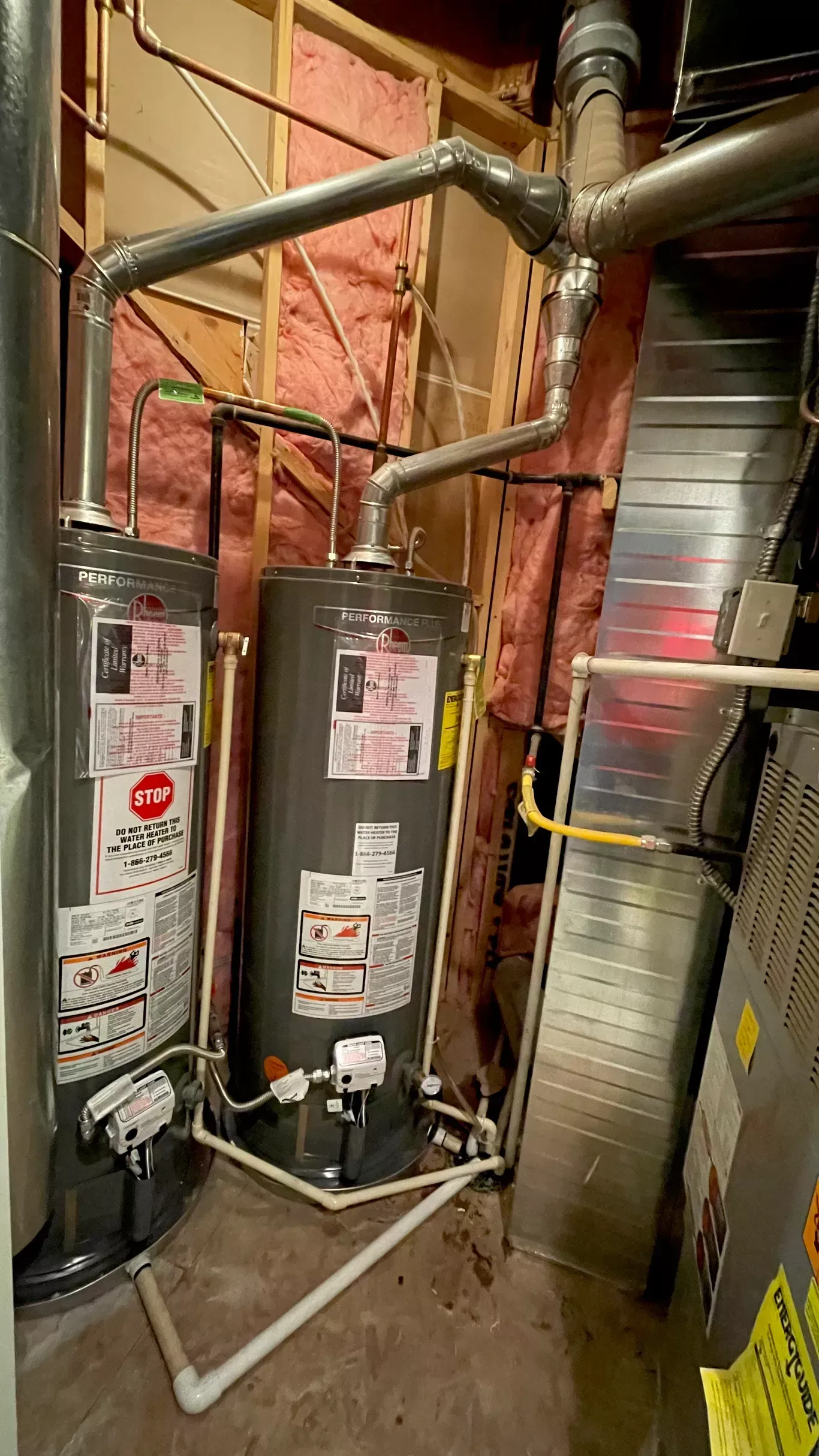 A water heater is sitting in a basement next to a furnace.