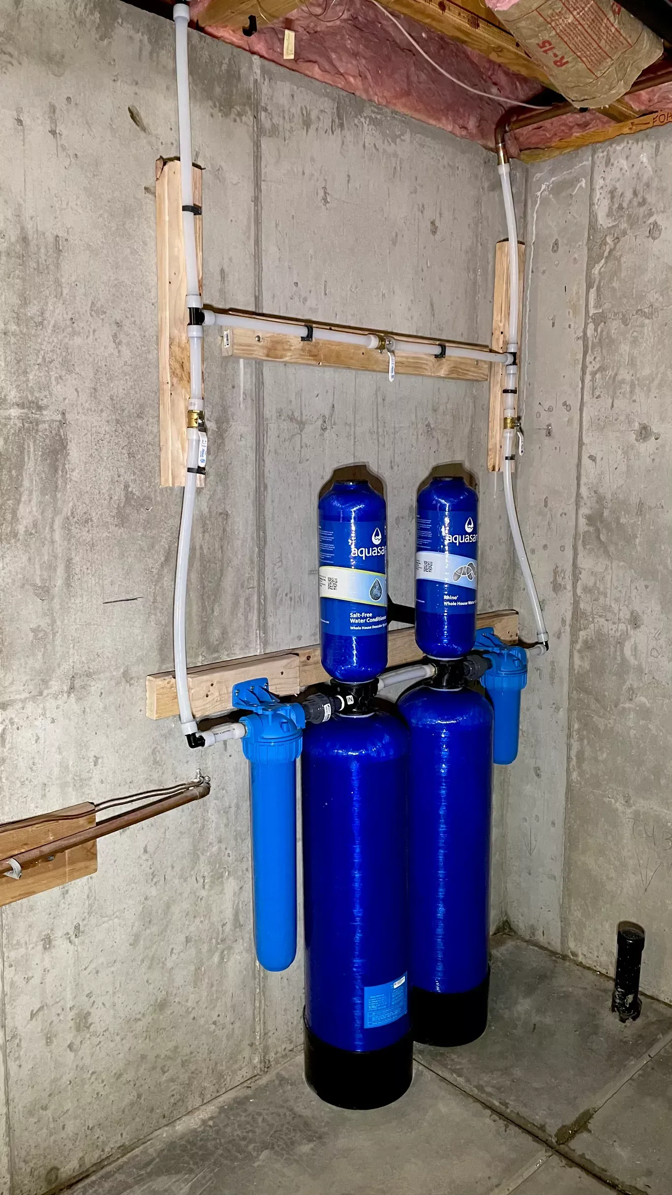 Two blue water filters are hanging on a wall in a basement.