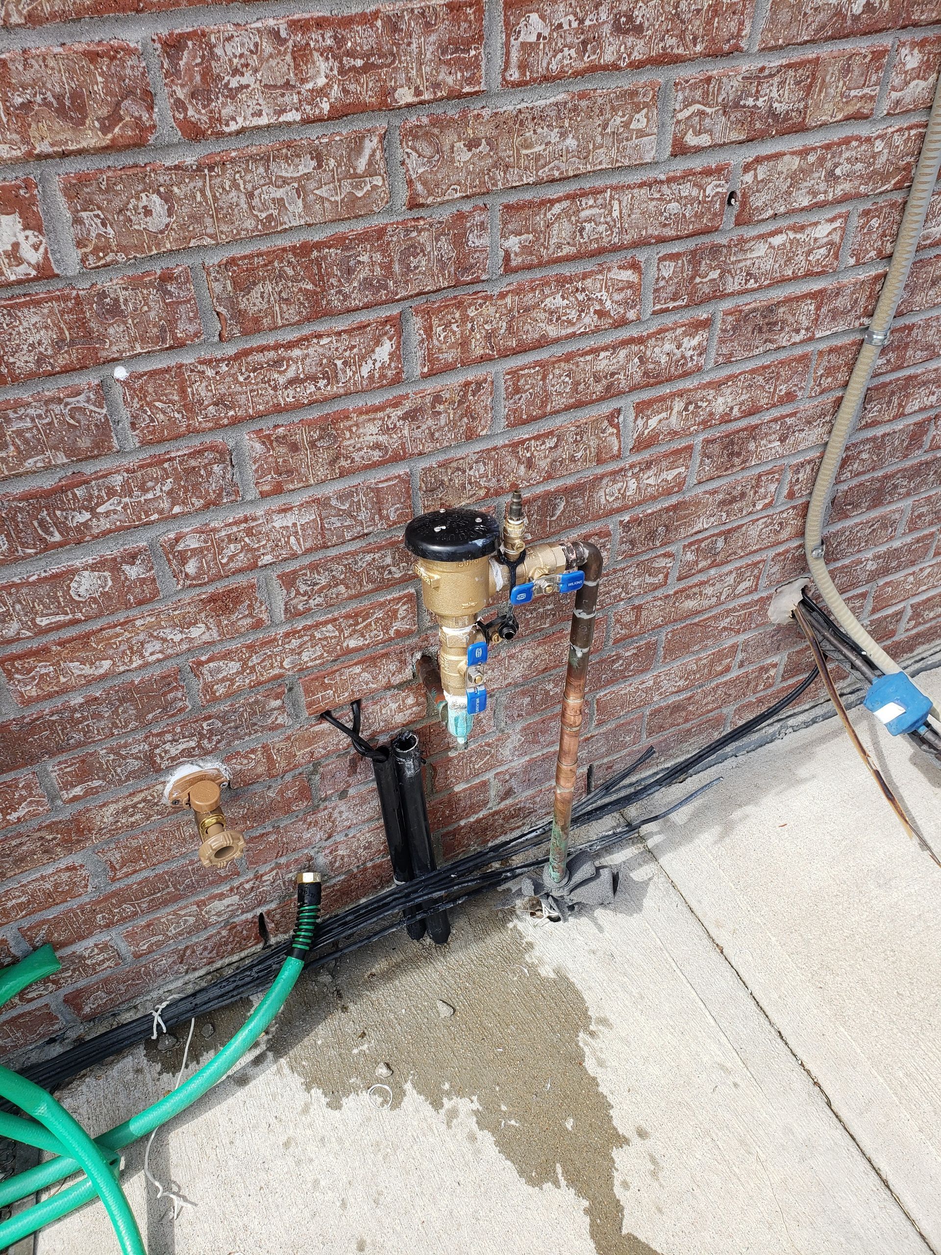 A hose is connected to a faucet on the side of a brick wall.