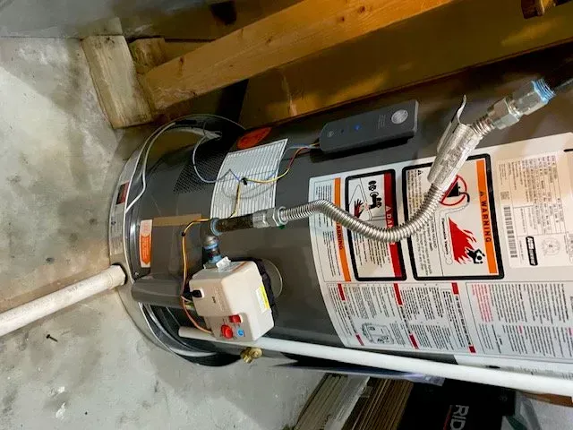 A water heater is sitting under a wooden beam in a garage.