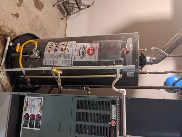 A water heater is sitting next to an air conditioner in a garage.