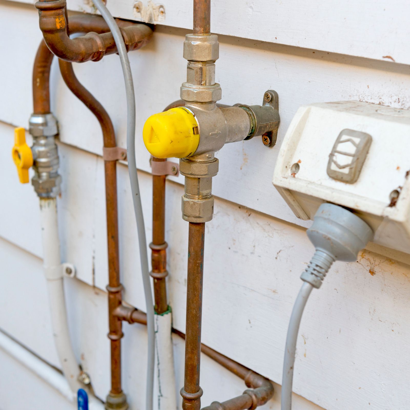 Pipes, gas valve, and electrical outlet on a white wall, some metal fixtures with a yellow component.