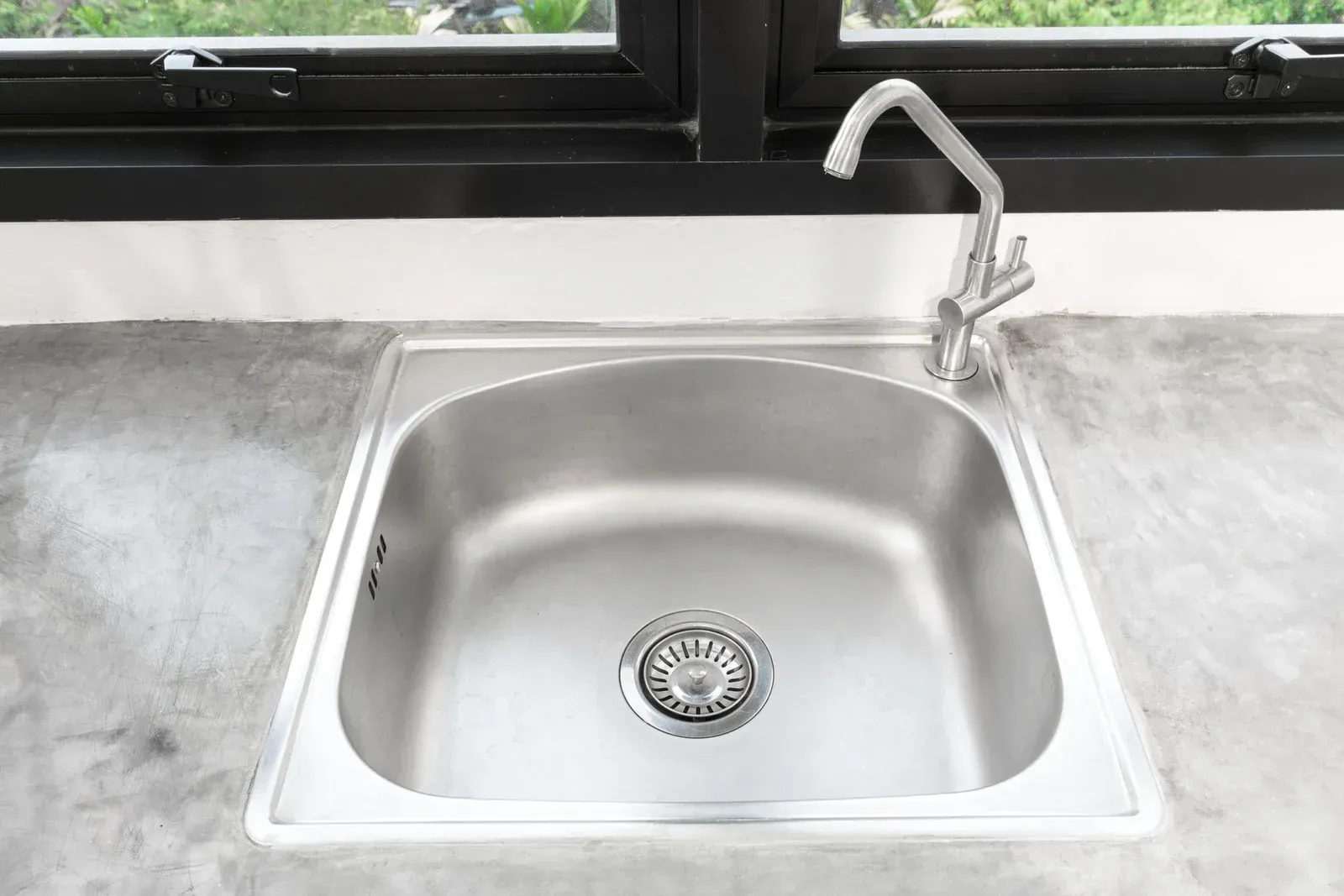 Stainless steel kitchen sink with faucet, set into a grey countertop, below a window.