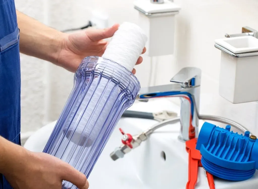 A person is holding a water filter in front of a sink.