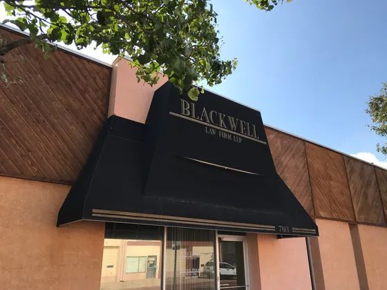 Blackwell Lounge entrance. Black awning over glass doors. Beige building with wood siding.