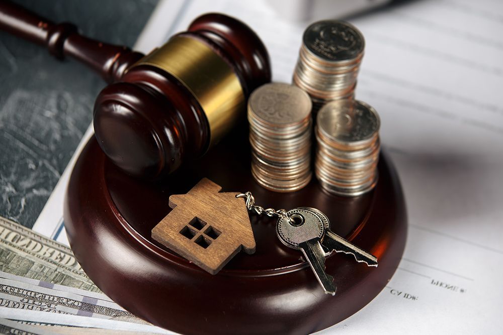 A judge 's gavel , keys , coins , and a small house are on a wooden block.