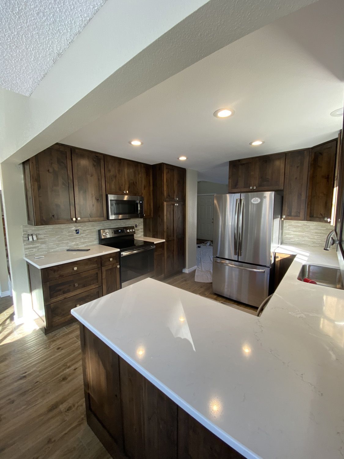 Modern kitchen with dark brown cabinets, white countertops, stainless steel appliances, and wood flooring.