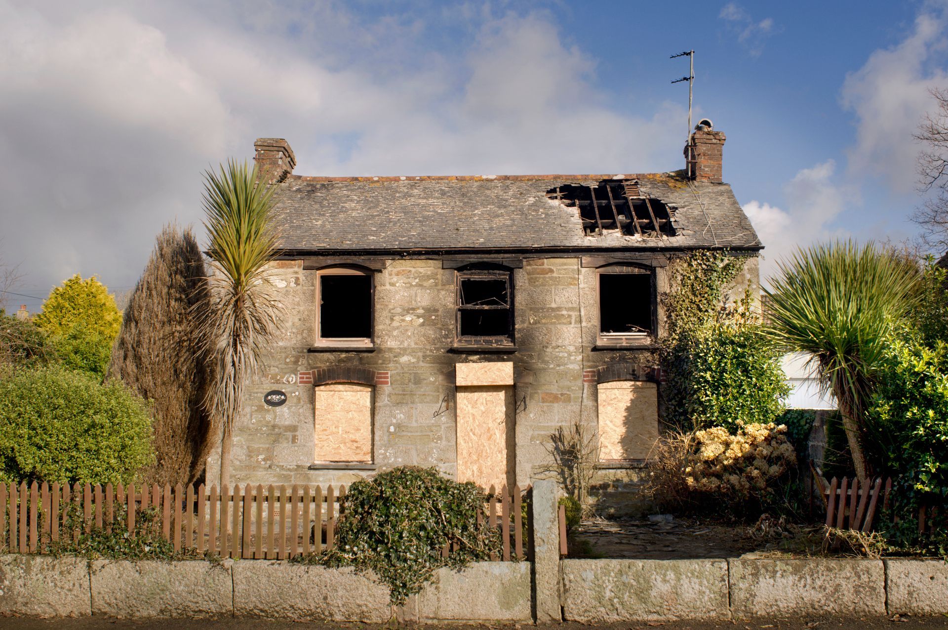 An old house with a broken roof and boarded up windows.