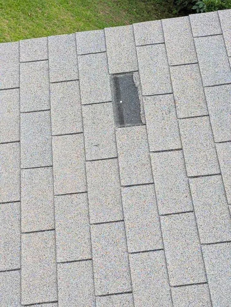 Gray asphalt roof with a missing shingle patched with black material.